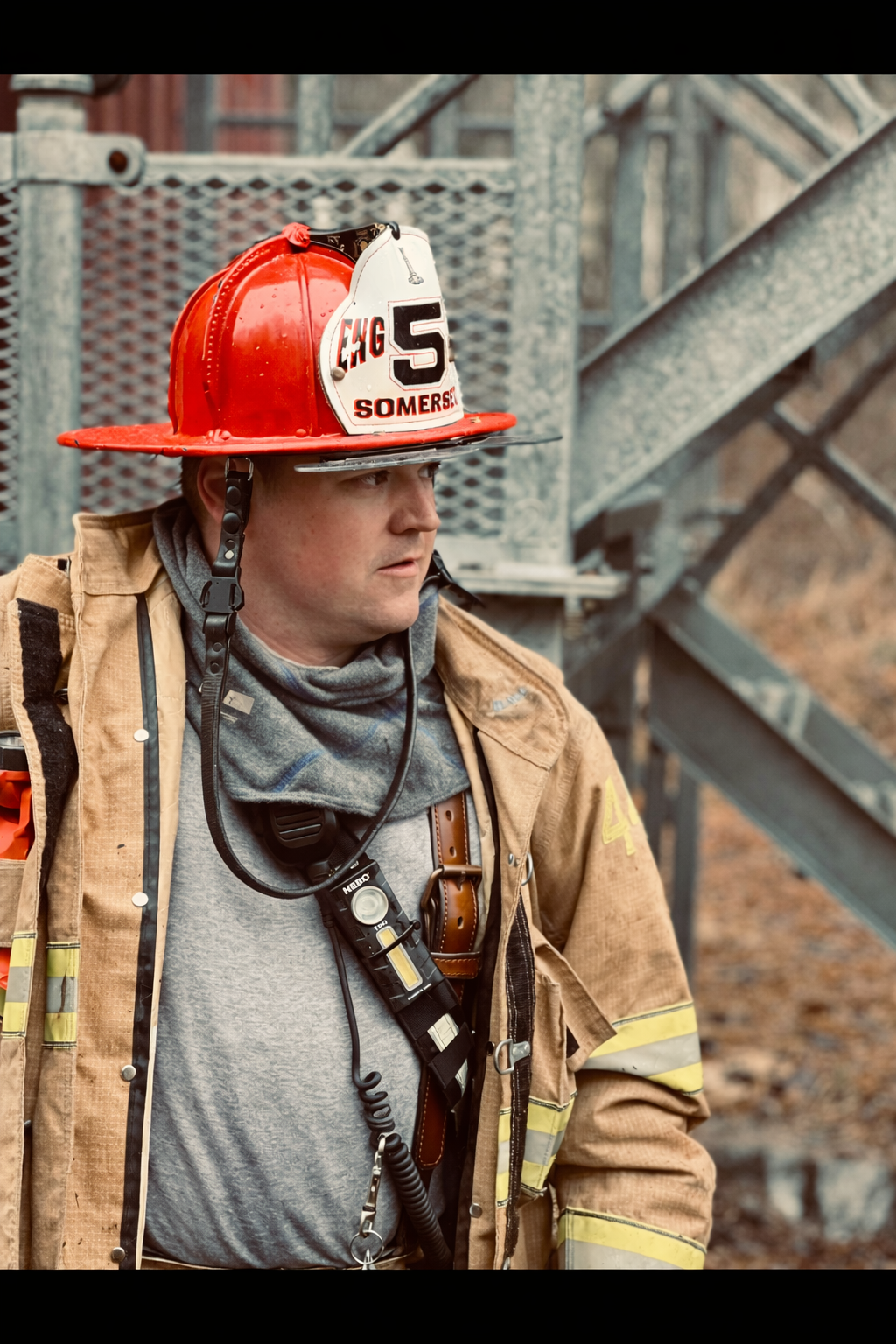 John Sulyma Jr. in full firefighter turnout gear and a red Somerset Engine 5 helmet, looking off-camera in a professional bio portrait.